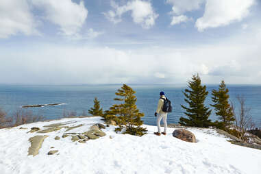 a hiker with a backpack standing at the top of a snowy mountain near the ocean