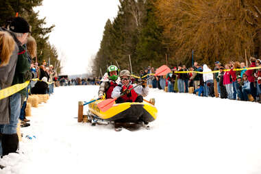 two people using a kayak mounted on skis as a racing vehicle on snow. they also have paddles.