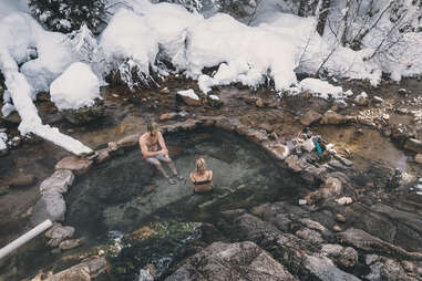 two people sitting in a rocky hot spring surrounded by snow