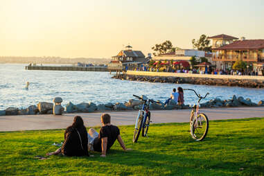 people with bikes sitting near a beautiful seaside town at sunset