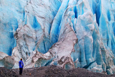 a tourist standing in front of an enormous, ancient glacier wall