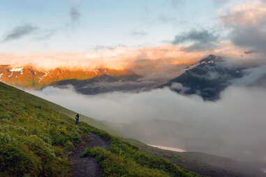 A lone hiker standing in the mist atop an Alaskan mountain at sunset