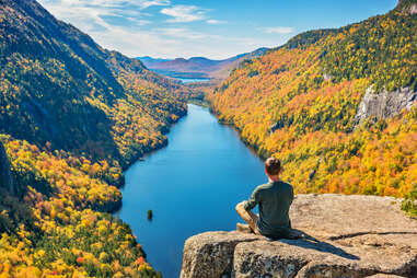 a hiker overlooking a forest, lake, and mountains