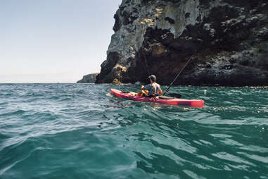 Young male sea kayaker fishing near cliff