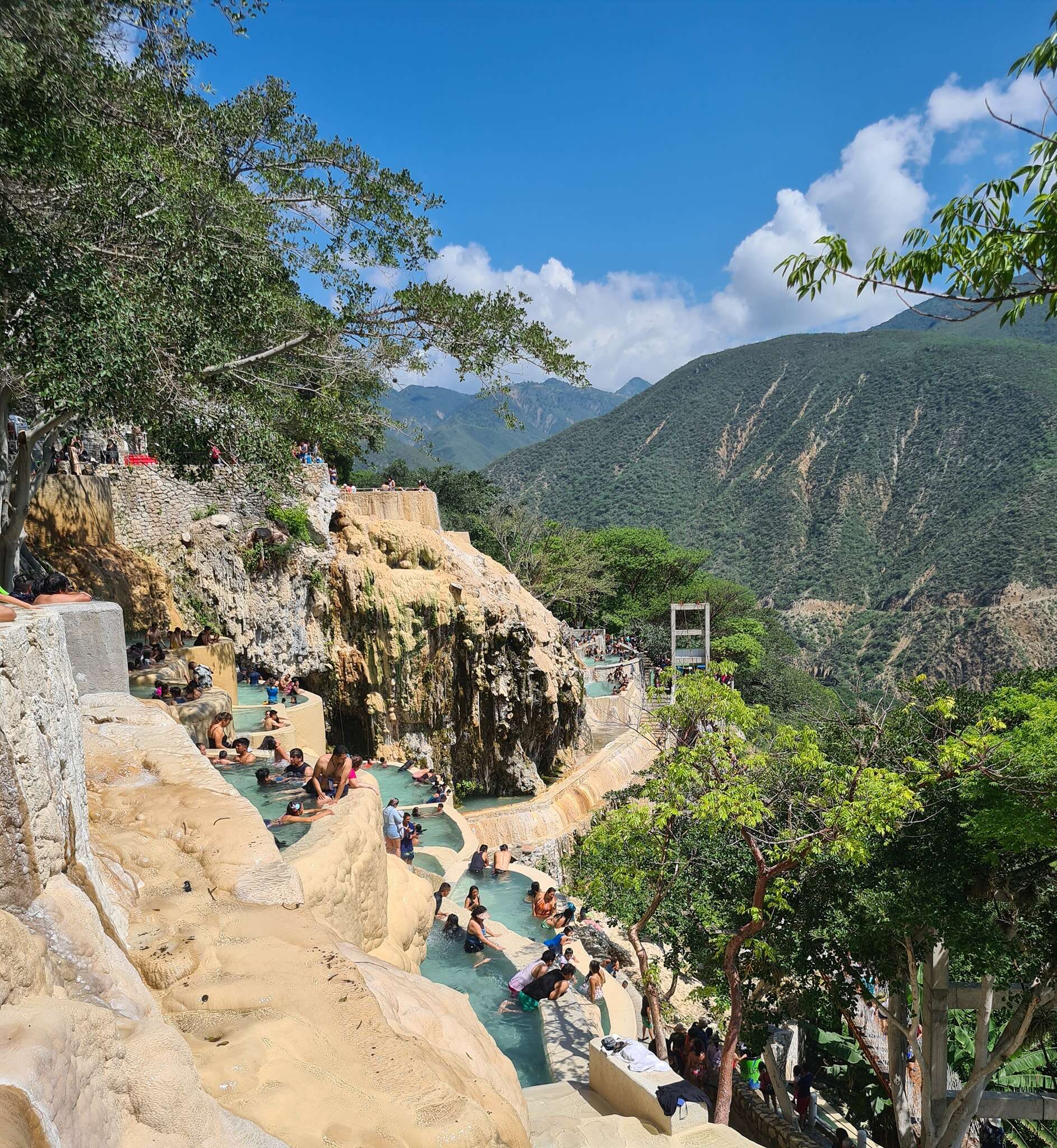 people in natural hot springs lining the side of a lush mountain