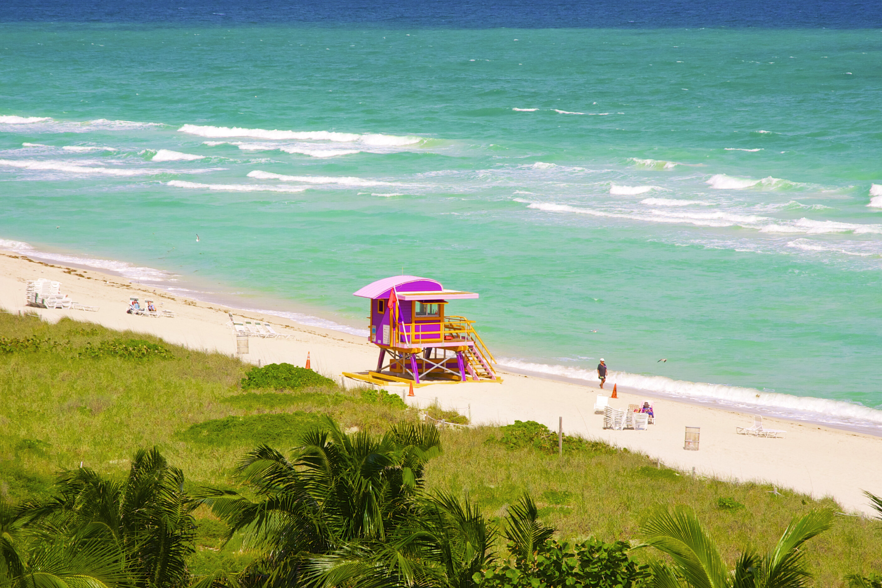 View from up high of pink and yellow wood lifeguard stand on white sand of Miami Beach