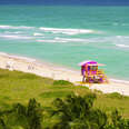 View from up high of pink and yellow wood lifeguard stand on white sand of Miami Beach