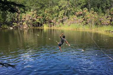 a person jumping off a swing into a lagoon