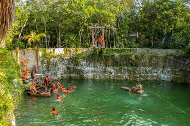 people in lifevests and one in a canoe hanging out on a cenote