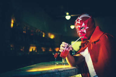 A Mexican luchador with red mask having a drink in a bar