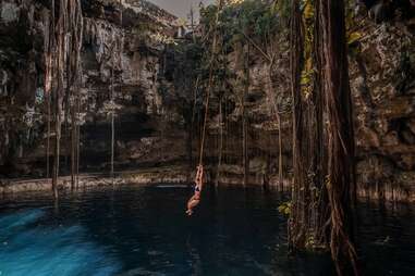 girl on rope swing above an underground natural pool