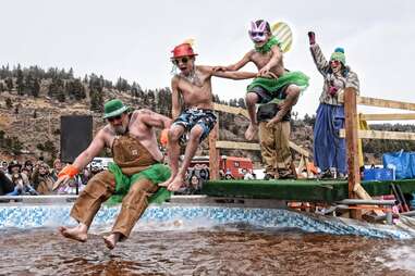 people in costume jumping into a vat of mud