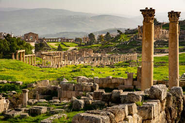 General view of the historical Roman site Gerasa in Jerash, Jordan, with pillars and Oval Plaza. Mountains and city in the far distance