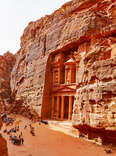 people walking past the ancient site of Petra carved into a mountain