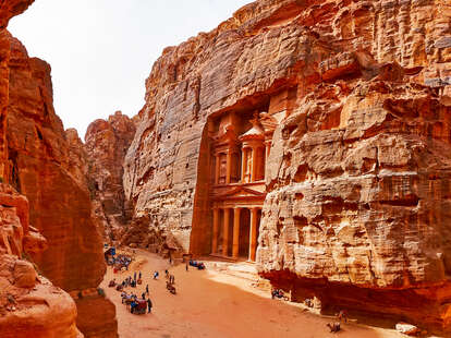 people walking past the ancient site of Petra carved into a mountain