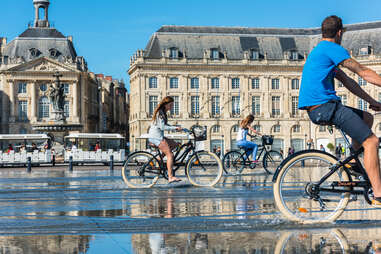 People riding bicycles in the mirror fountain in front of Place de la Bourse 