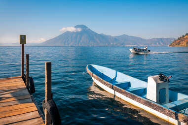 View of Volcano San Pedro from the shore of Lake Atitlan in Guatemala with a tourist boat docked at a pier for a stop over at a secluded resort on the shore of the lake