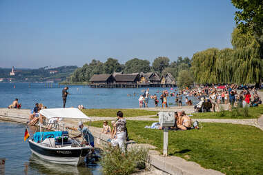 people on grass, a dock, and a lakeshore near beautiful trees and a cabin