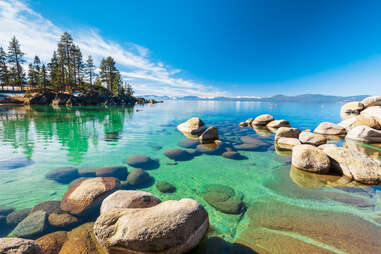 Lake Tahoe rocky shoreline in sunny day, beach with blue sky over clear transparent water