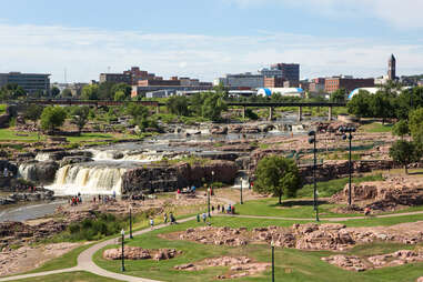 Tourists visit the waterfalls of Falls Park in Sioux Falls, South Dakota, with city skyline in the background