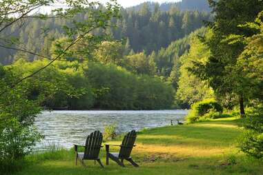 two lawn chairs sitting near a lake surrounded by dense forest
