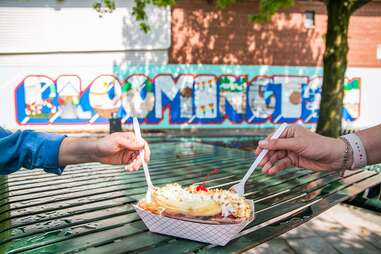 two hands getting ready to dig into a banana split sundae with a mural in the background