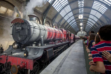 people in a train station watching as a steam locomotive rolls in