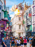 people walking through a magical city street with a fire breathing dragon above