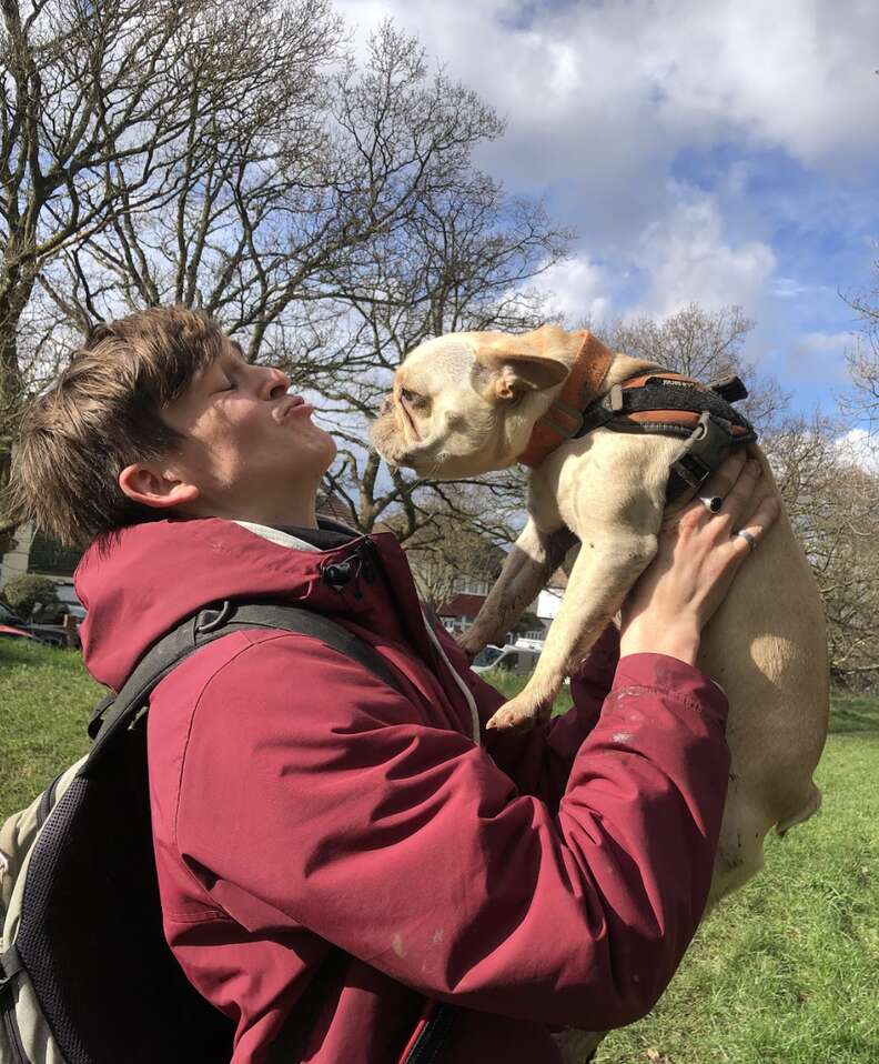 Dog walker holds a pug in the air and kisses him.