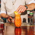 a bartender putting a garnish on a colada cocktail in a pineapple glassware.