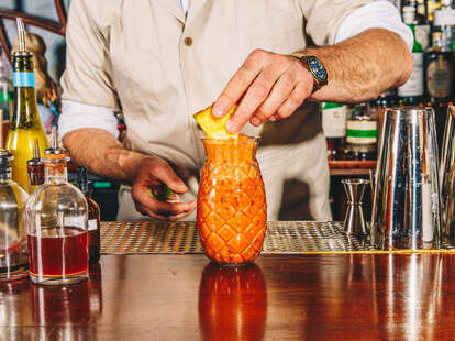 a bartender putting a garnish on a colada cocktail in a pineapple glassware.