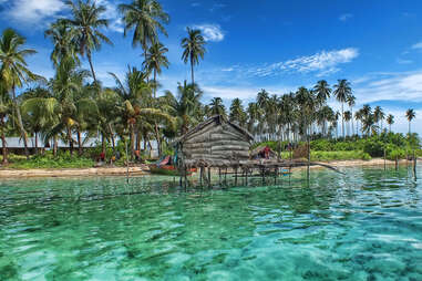 small hut on the water with palm trees in the background