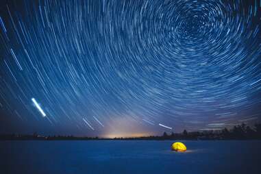 Tent lit up at night in the snow and spiral stars in the sky