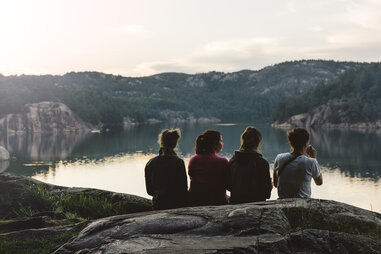 four people sitting on rocks by lake