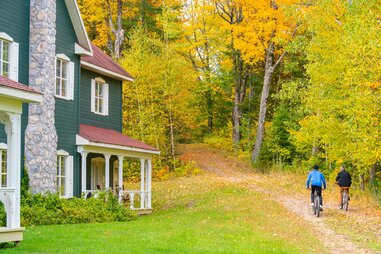 two people biking through forest surrounding cabin
