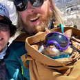 couple in skiing gear with a cat in bag wearing ski goggles