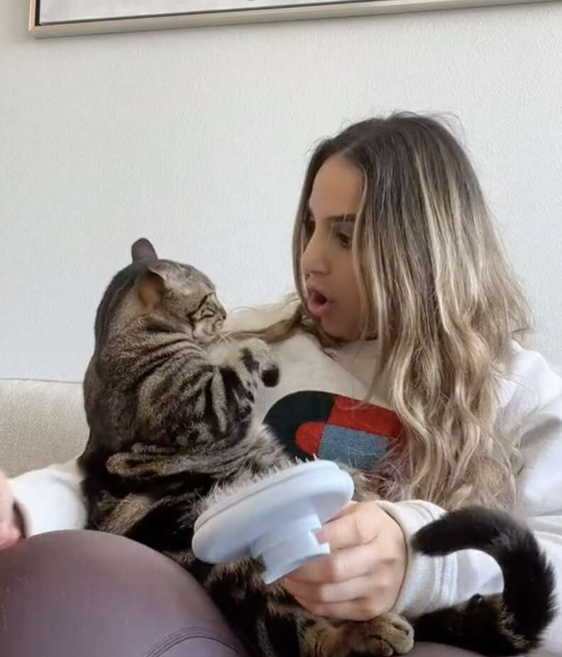 A woman acts surprised by her cat's reaction.