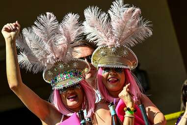 Two women with pic hair and feathered hats celebrating.