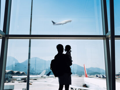 A father holds his child while watching a plane through the window at an airport as airlines revise their family seating policies