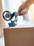 A person closes a cardboard box using packing tape