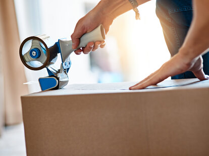 A person closes a cardboard box using packing tape