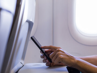 Hands using a mobile phone on an airplane.