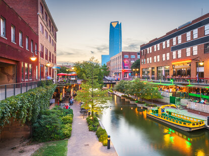 Oklahoma City’s Bricktown at Dusk. Sidewalk next to small waterway and lots of colorful lighting.