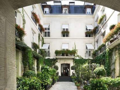 A courtyard in Paris, covered in vines and greenery with large french windows.