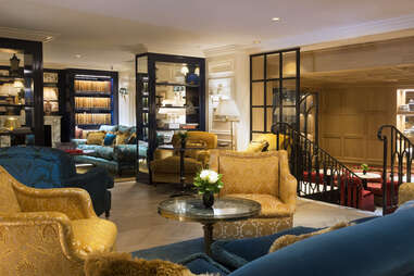 A lobby with gold and royal blue chairs, bookshelves, and expensive decor.