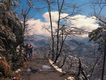 Two hikers pause on a trail to look out over the Great Smoky Mountains