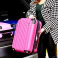A woman putting a bright pink carry-on suitcase without wheels into the back of a vehicle.