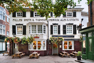 The exterior of the Crown & Anchor pub, which is a colonial style building with benches out front. 