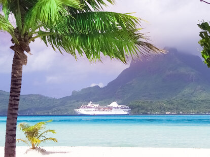 The beach on Motu island off the coast of Bora Bora with island mountain and cruise ship in background