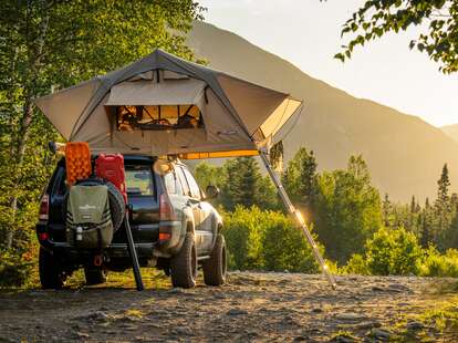 A campsite in the woods, with a tent set up on the roof of a car. 
